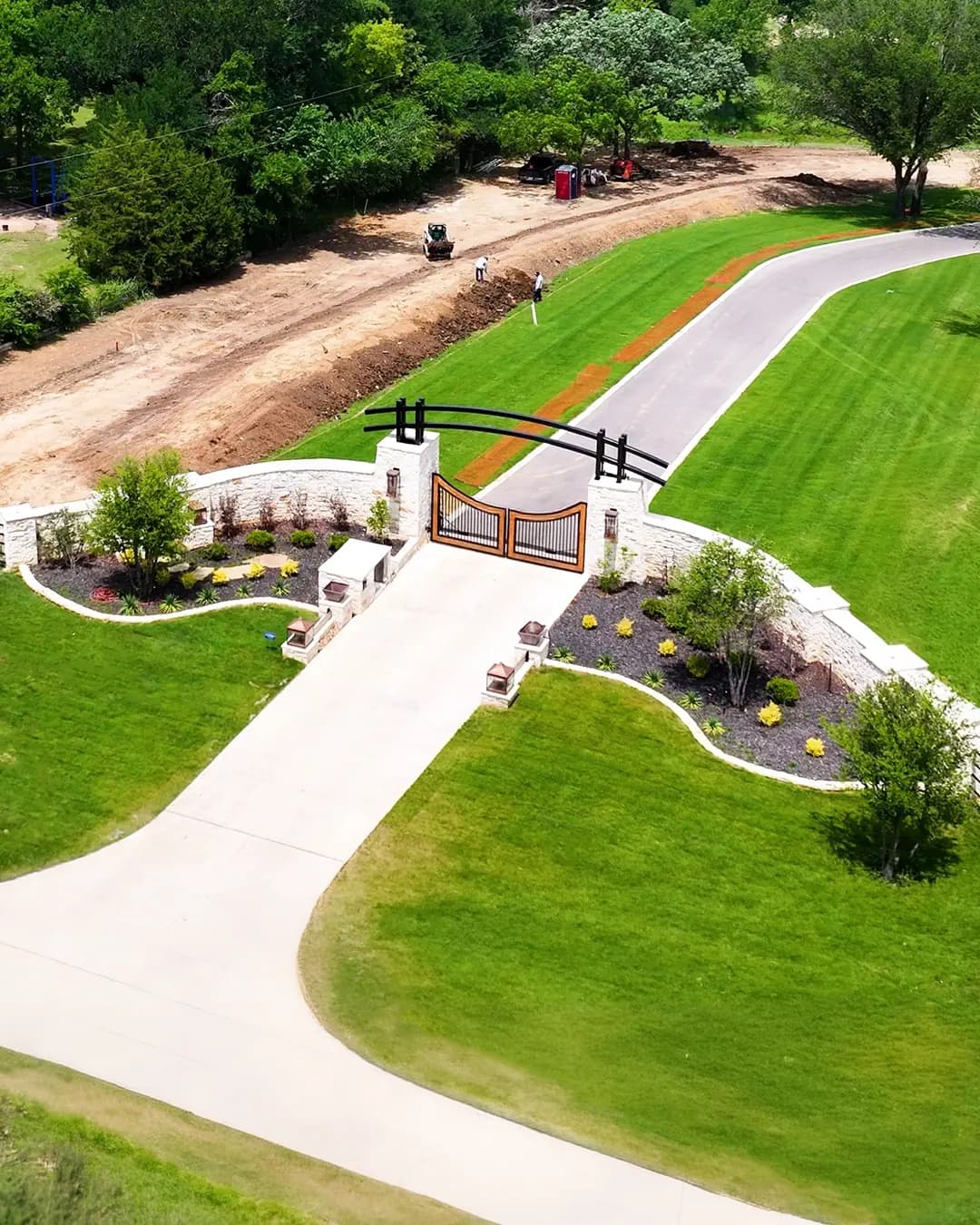Aerial view of a custom stone entry gate and driveway framed by fresh landscaping and lawn on a Colleyville property